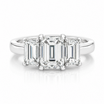 A three-stone diamond engagement ring featuring an emerald-cut center stone and baguette-cut side stones in a platinum metal setting, shown on a clean white background with a soft reflection.