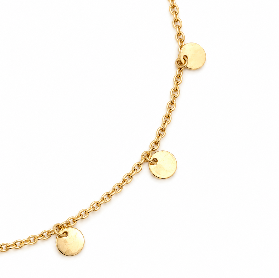 Close-up of polished gold disc drops suspended from a 9ct yellow gold trace link bracelet.