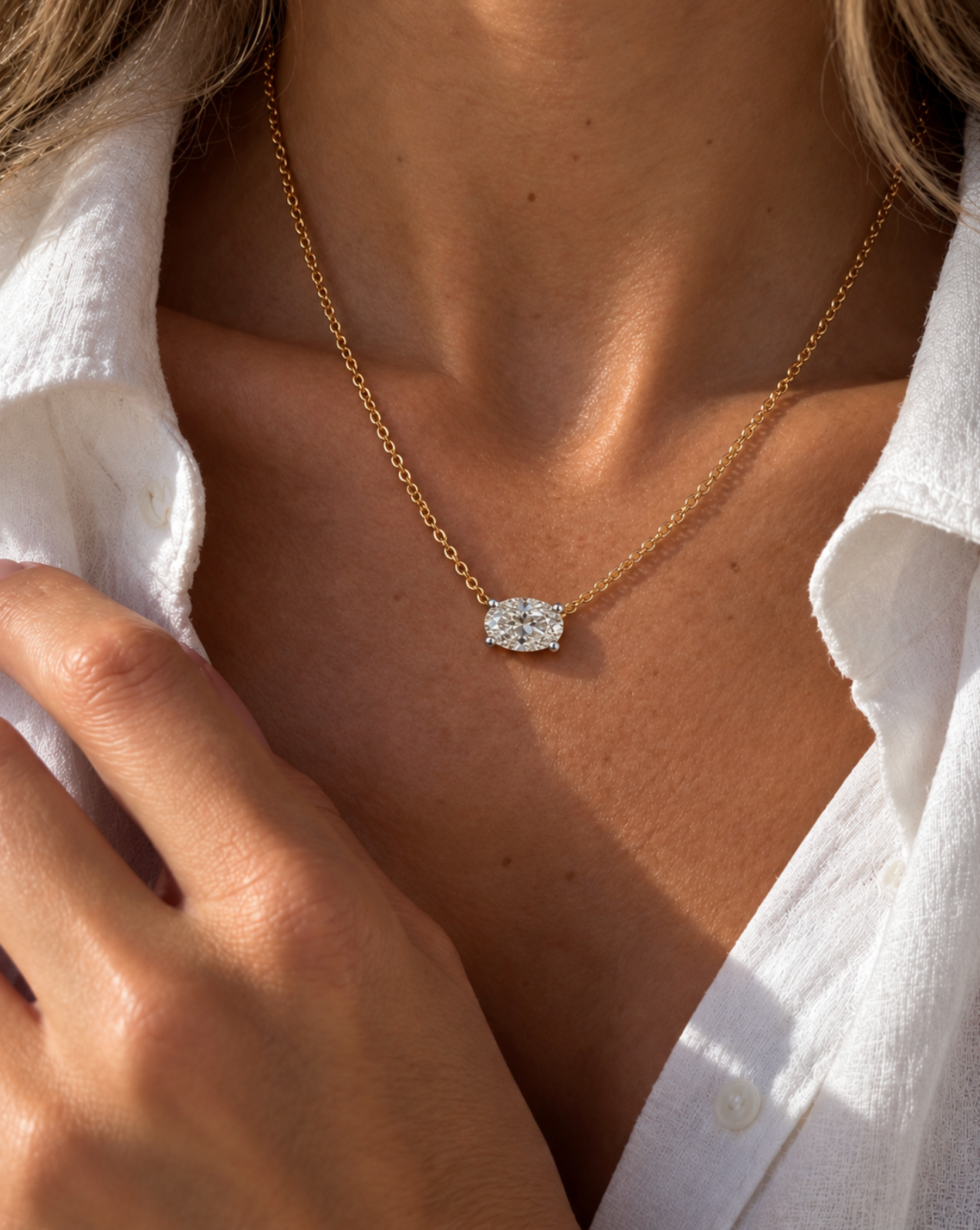 A close-up lifestyle shot of a woman wearing a delicate gold chain necklace with a oval diamond pendant, styled with a white button-down shirt.