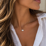 A close-up lifestyle shot of a woman wearing a delicate gold chain necklace with a pear cut diamond pendant, styled with a white button-down shirt.