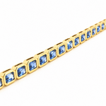 A yellow gold tennis bracelet featuring a row of emerald-cut sapphires, displayed on a clean white background.