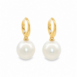 A pair of gold huggie hoop earrings with large, lustrous white South Sea pearls hanging from gold posts, shown on a clean white background.
