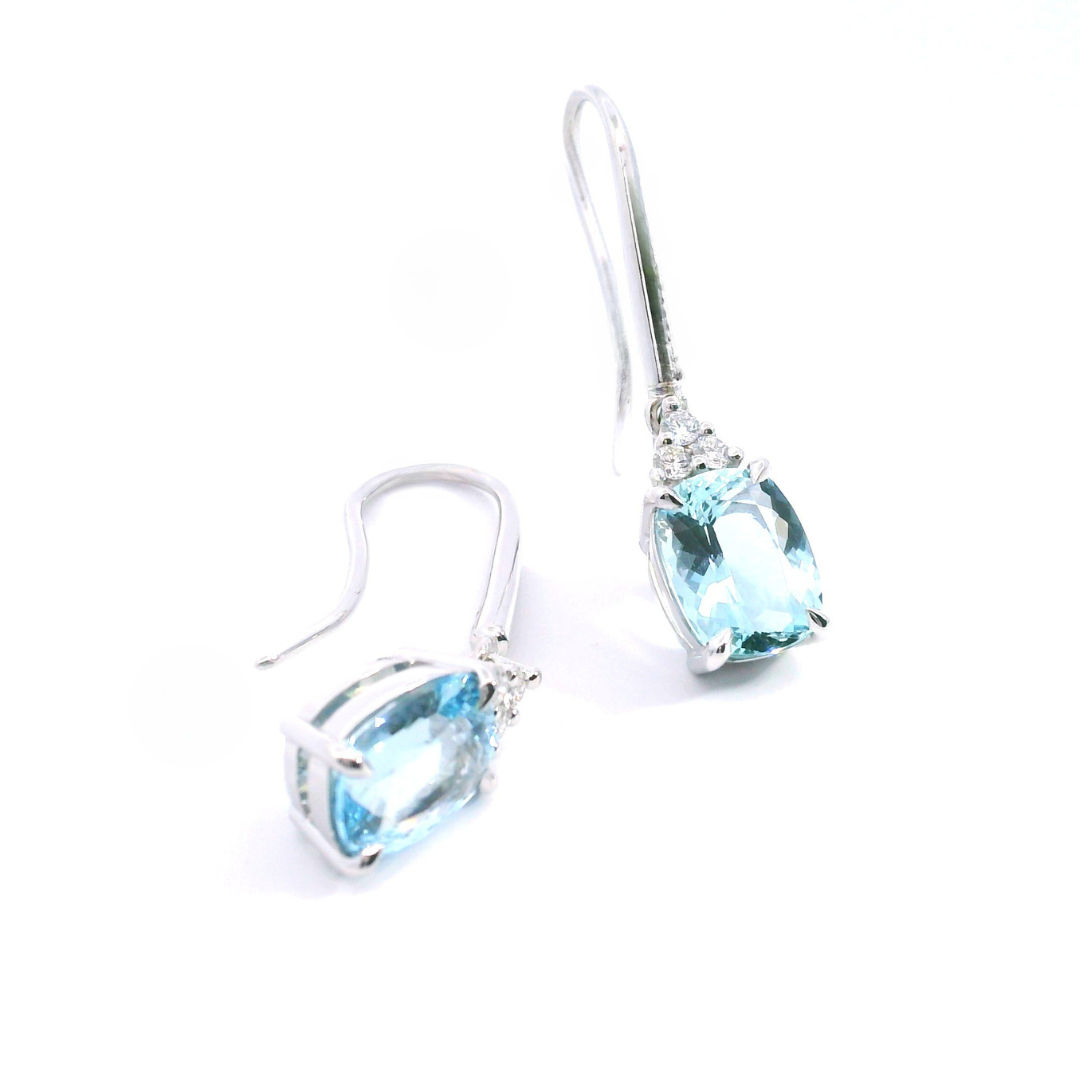 18ct white gold aquamarine and diamond drop earrings featuring cushion cut aquamarines suspended from triangular diamond clusters with articulated hook fittings.