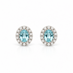 18ct white gold aquamarine and diamond halo stud earrings featuring oval-cut blue aquamarines surrounded by round brilliant cut diamonds.