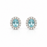 18ct white gold aquamarine and diamond halo stud earrings featuring oval-cut blue aquamarines surrounded by round brilliant cut diamonds.