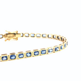 18ct yellow gold blue sapphire bracelet featuring articulated octagonal links with bezel-set emerald cut sapphires.