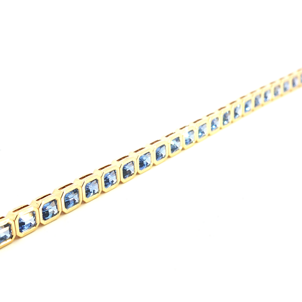 18ct yellow gold blue sapphire bracelet featuring articulated octagonal links with bezel-set emerald cut sapphires.