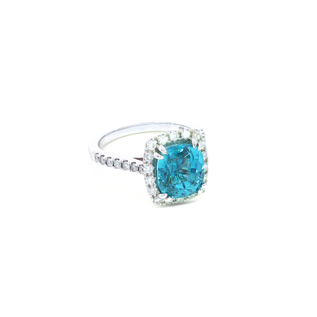 18ct white gold ring featuring a 5.23ct cushion cut blue zircon in a double talon claw setting surrounded by a diamond halo and shoulders.