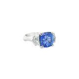18ct white gold three stone ring featuring an 8.07ct cushion cut blue sapphire with cadillac cut diamond side stones and sapphire-diamond accents in the undercarriage.