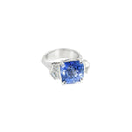 18ct white gold three stone ring featuring an 8.07ct cushion cut blue sapphire with cadillac cut diamond side stones and sapphire-diamond accents in the undercarriage.