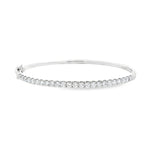 18ct white gold diamond bangle featuring claw-set round brilliant cut diamonds across the top, hinged oval profile with slide catch and safety clasps.