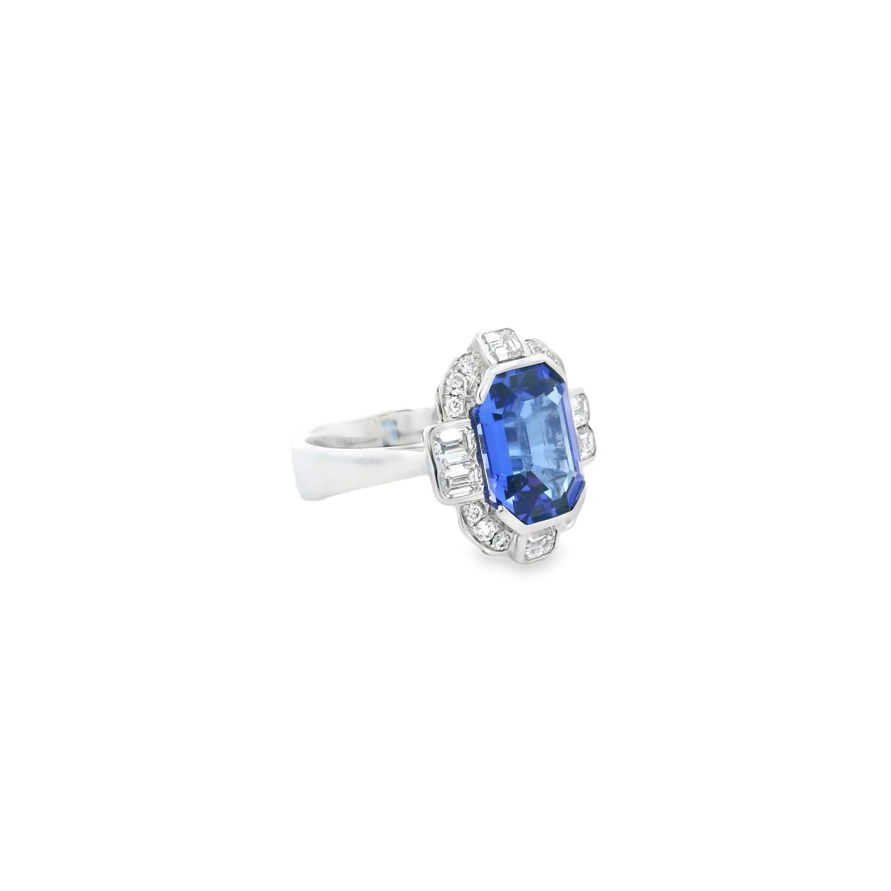18ct white gold ring featuring a 5.11ct emerald cut tanzanite framed by emerald and round brilliant cut diamonds in a detailed halo setting with upswept shoulders.