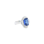 18ct white gold ring featuring a 5.11ct emerald cut tanzanite framed by emerald and round brilliant cut diamonds in a detailed halo setting with upswept shoulders.