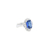 18ct white gold ring featuring a 5.11ct emerald cut tanzanite framed by emerald and round brilliant cut diamonds in a detailed halo setting with upswept shoulders.