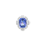 18ct white gold ring featuring a 5.11ct emerald cut tanzanite framed by emerald and round brilliant cut diamonds in a detailed halo setting with upswept shoulders.