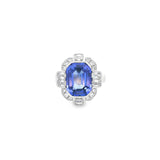 18ct white gold ring featuring a 5.11ct emerald cut tanzanite framed by emerald and round brilliant cut diamonds in a detailed halo setting with upswept shoulders.