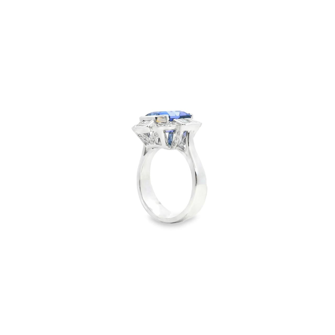 18ct white gold ring featuring a 5.11ct emerald cut tanzanite framed by emerald and round brilliant cut diamonds in a detailed halo setting with upswept shoulders.