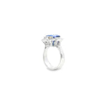 18ct white gold ring featuring a 5.11ct emerald cut tanzanite framed by emerald and round brilliant cut diamonds in a detailed halo setting with upswept shoulders.