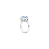 18ct white gold ring featuring a 5.11ct emerald cut tanzanite framed by emerald and round brilliant cut diamonds in a detailed halo setting with upswept shoulders.