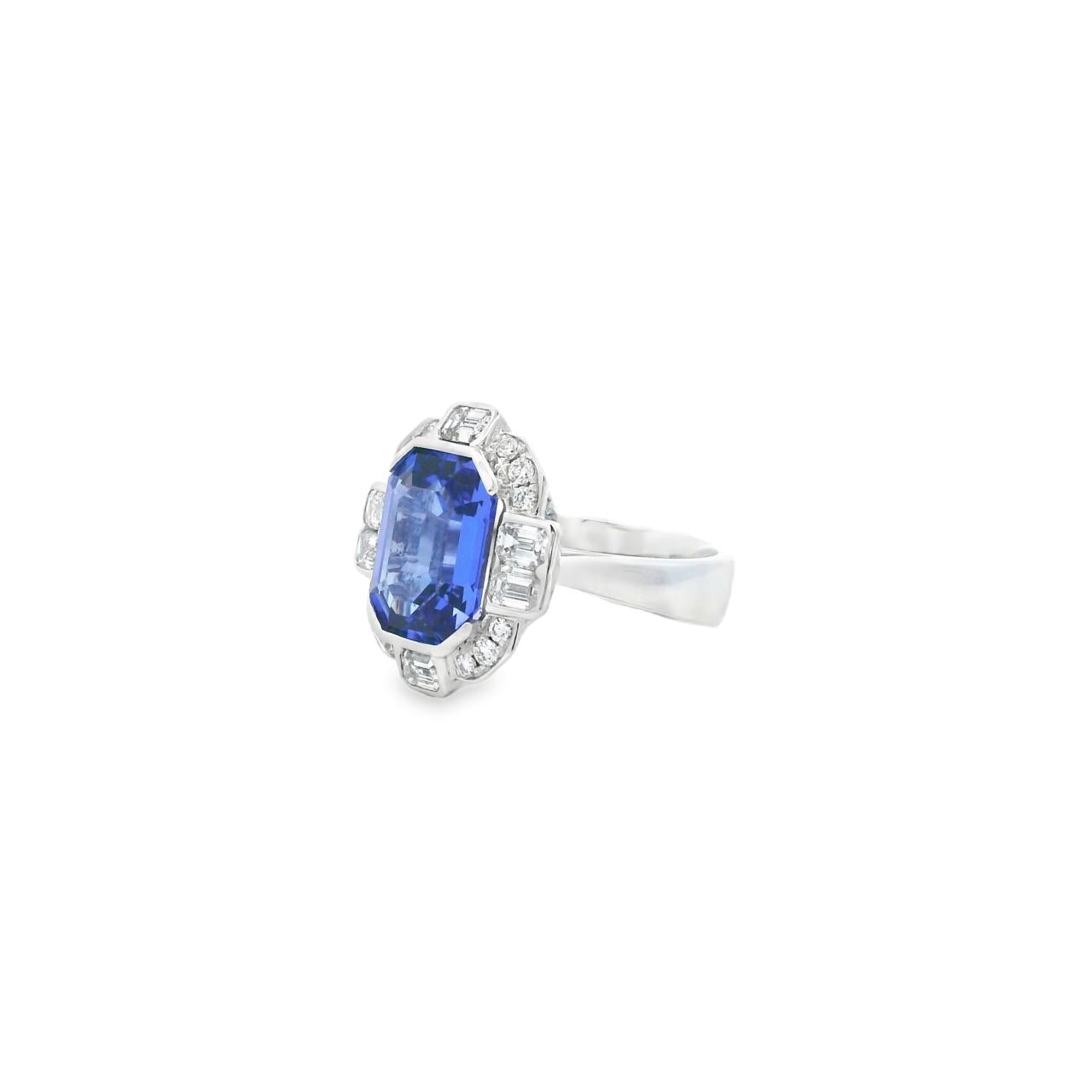 18ct white gold ring featuring a 5.11ct emerald cut tanzanite framed by emerald and round brilliant cut diamonds in a detailed halo setting with upswept shoulders.