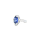 18ct white gold ring featuring a 5.11ct emerald cut tanzanite framed by emerald and round brilliant cut diamonds in a detailed halo setting with upswept shoulders.