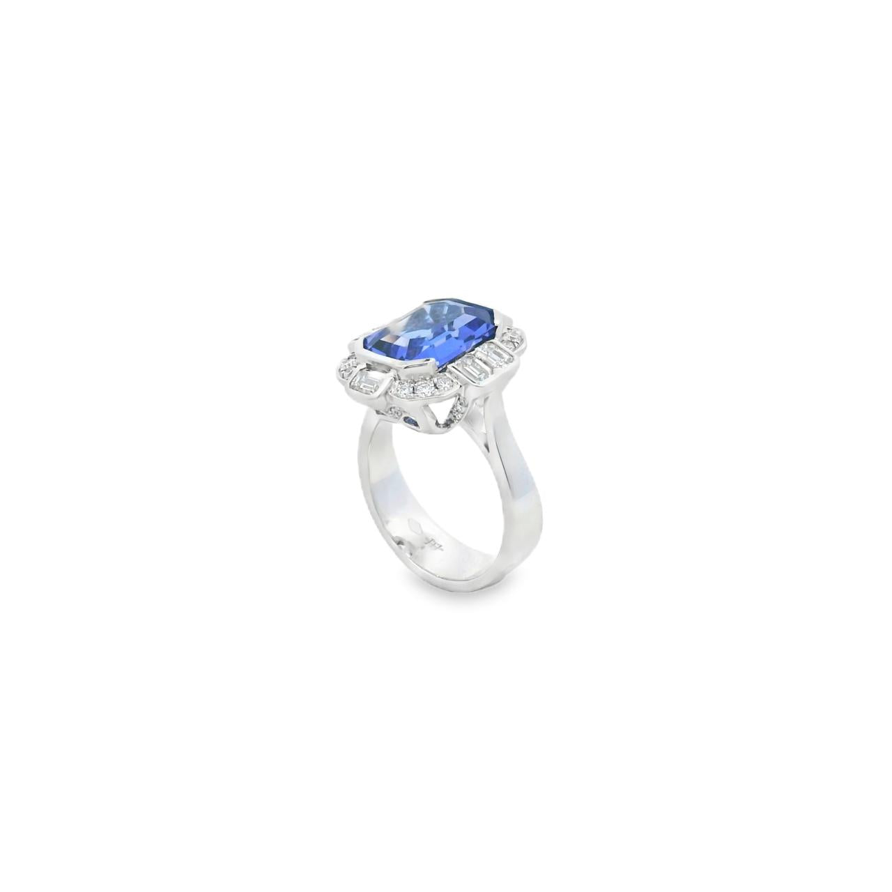 18ct white gold ring featuring a 5.11ct emerald cut tanzanite framed by emerald and round brilliant cut diamonds in a detailed halo setting with upswept shoulders.