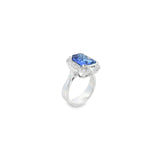 18ct white gold ring featuring a 5.11ct emerald cut tanzanite framed by emerald and round brilliant cut diamonds in a detailed halo setting with upswept shoulders.