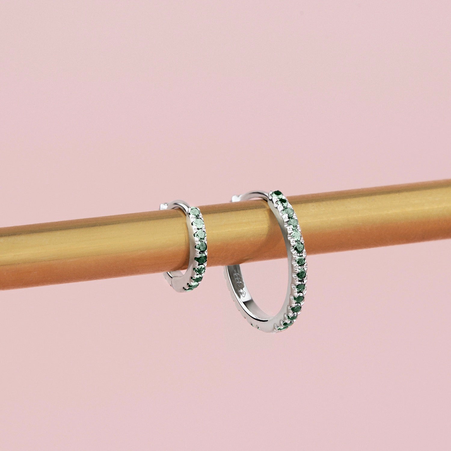18ct white gold huggie earrings featuring claw-set emeralds along the front and back, medium size with 11mm inside diameter and hinged fittings.