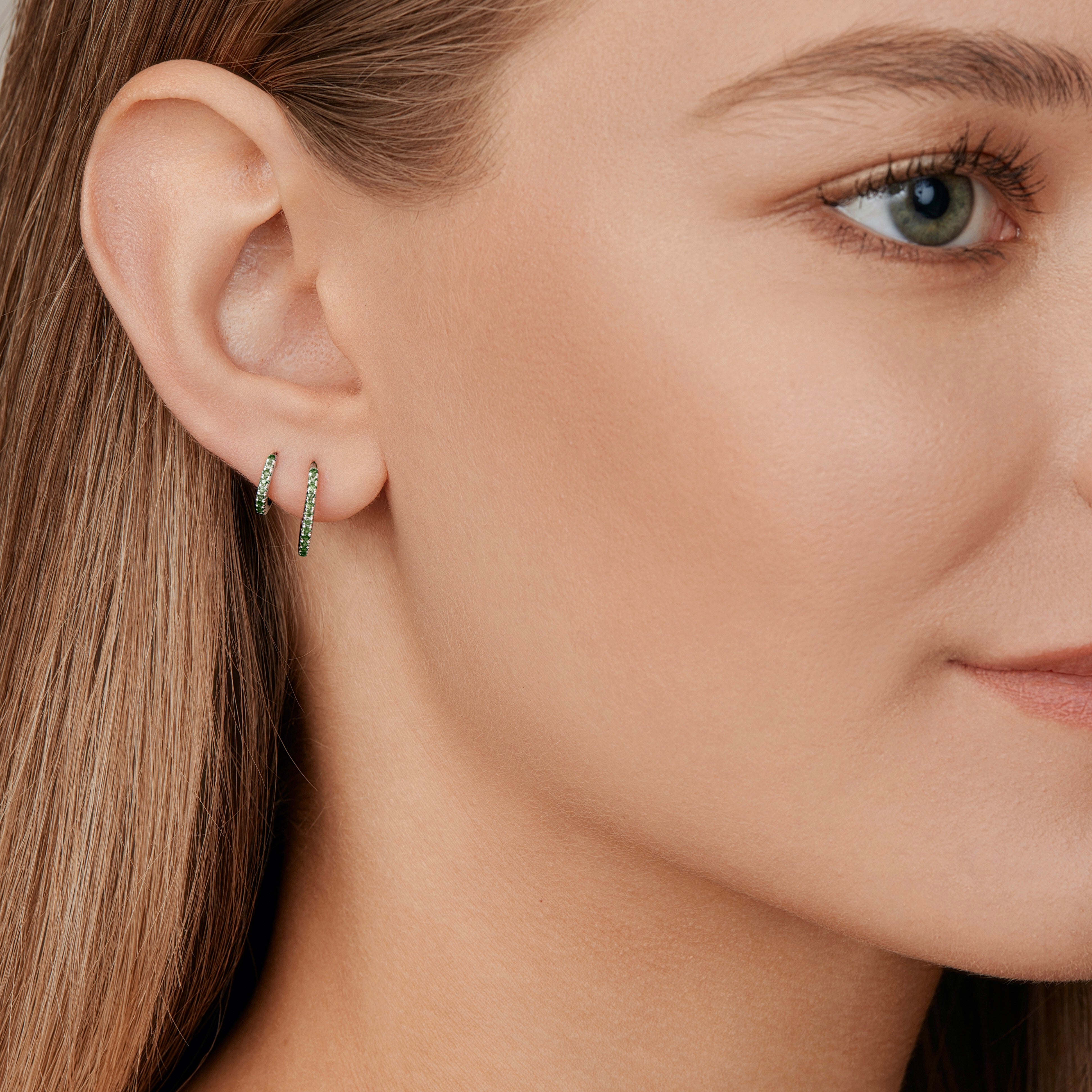 18ct white gold huggie earrings featuring claw-set emeralds along the front and back, medium size with 11mm inside diameter and hinged fittings.