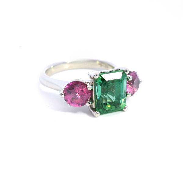 Platinum three-stone ring featuring a 2.68ct emerald cut green tourmaline with two round cut pink spinels in tiered claw settings.