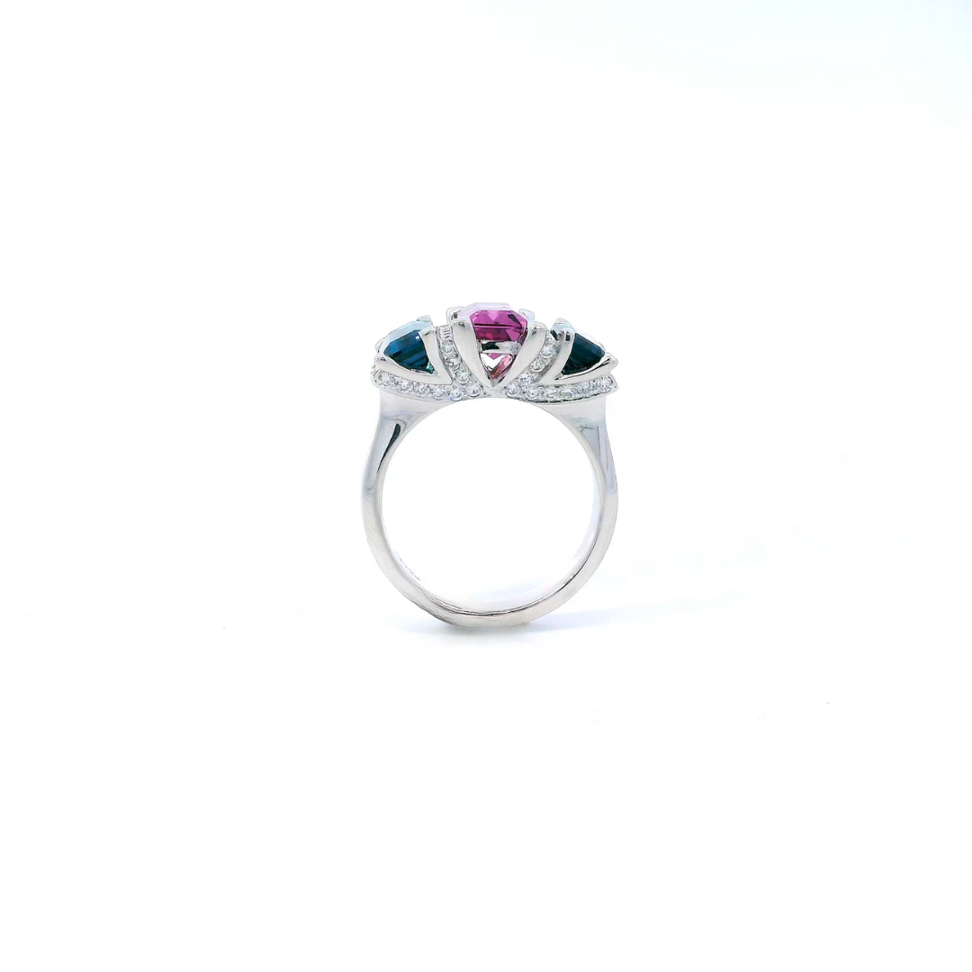 18ct white gold ring featuring a 2.11ct emerald cut purple-pink Malaia garnet with two greenish-blue tourmalines and diamond-set tiered claw and bar details.