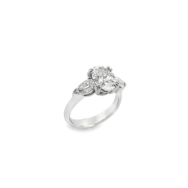 18ct white gold three stone diamond ring featuring a 2.17ct oval centre diamond with pear cut diamond side stones in tiered cap-and-claw settings.