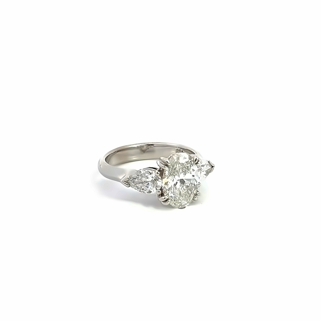 18ct white gold three stone diamond ring featuring a 2.17ct oval centre diamond with pear cut diamond side stones in tiered cap-and-claw settings.