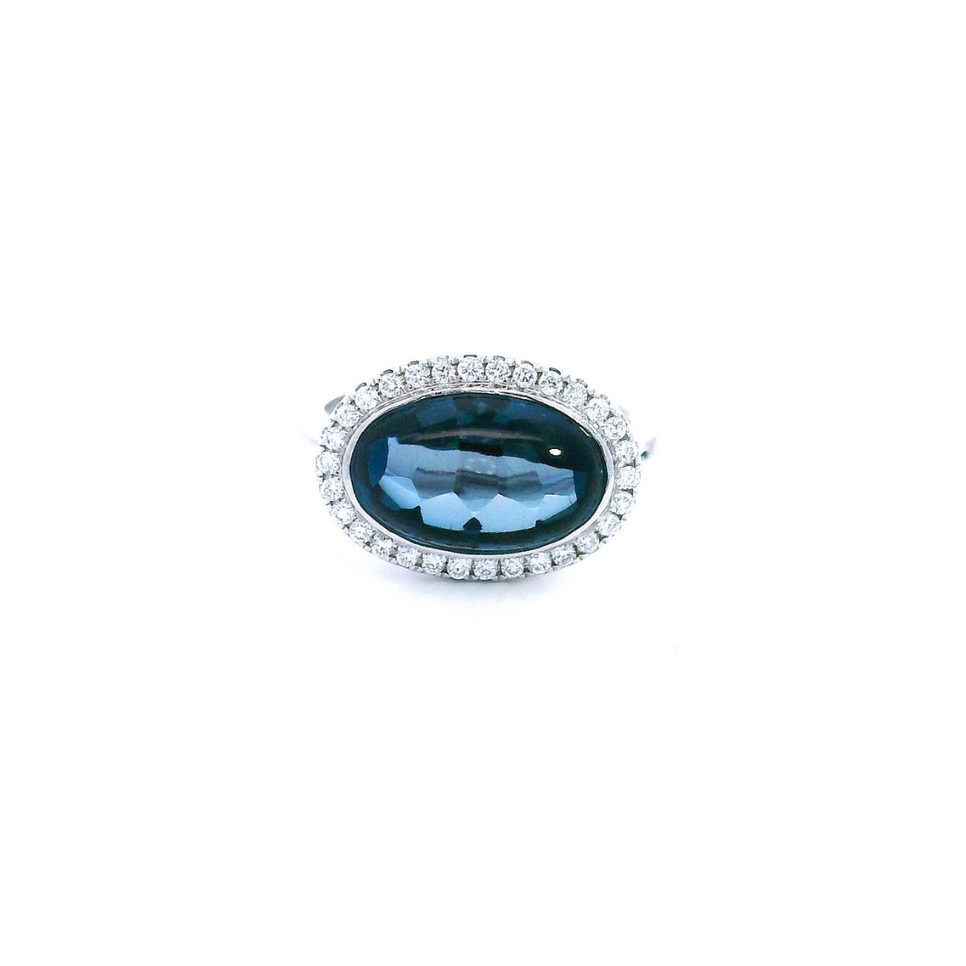 18ct white gold ring featuring a 5.83ct oval cabochon cut London blue topaz in a horizontal bezel setting with a halo of round brilliant cut diamonds.