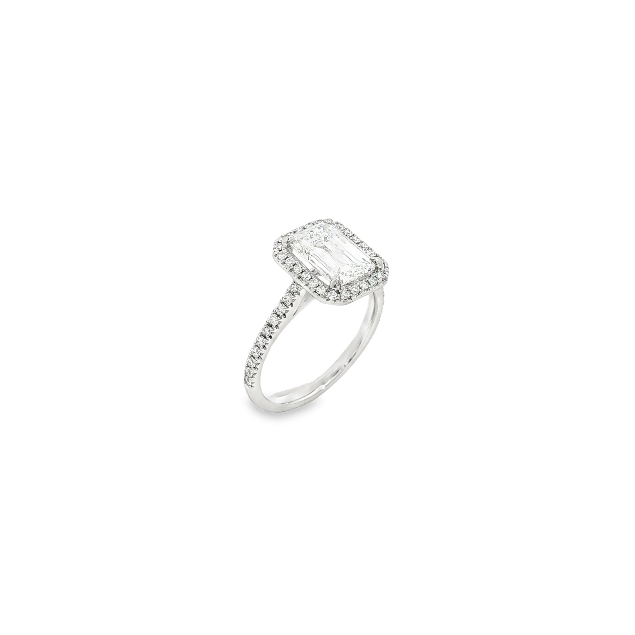 Platinum emerald cut diamond ring with halo and diamond-set shoulders.