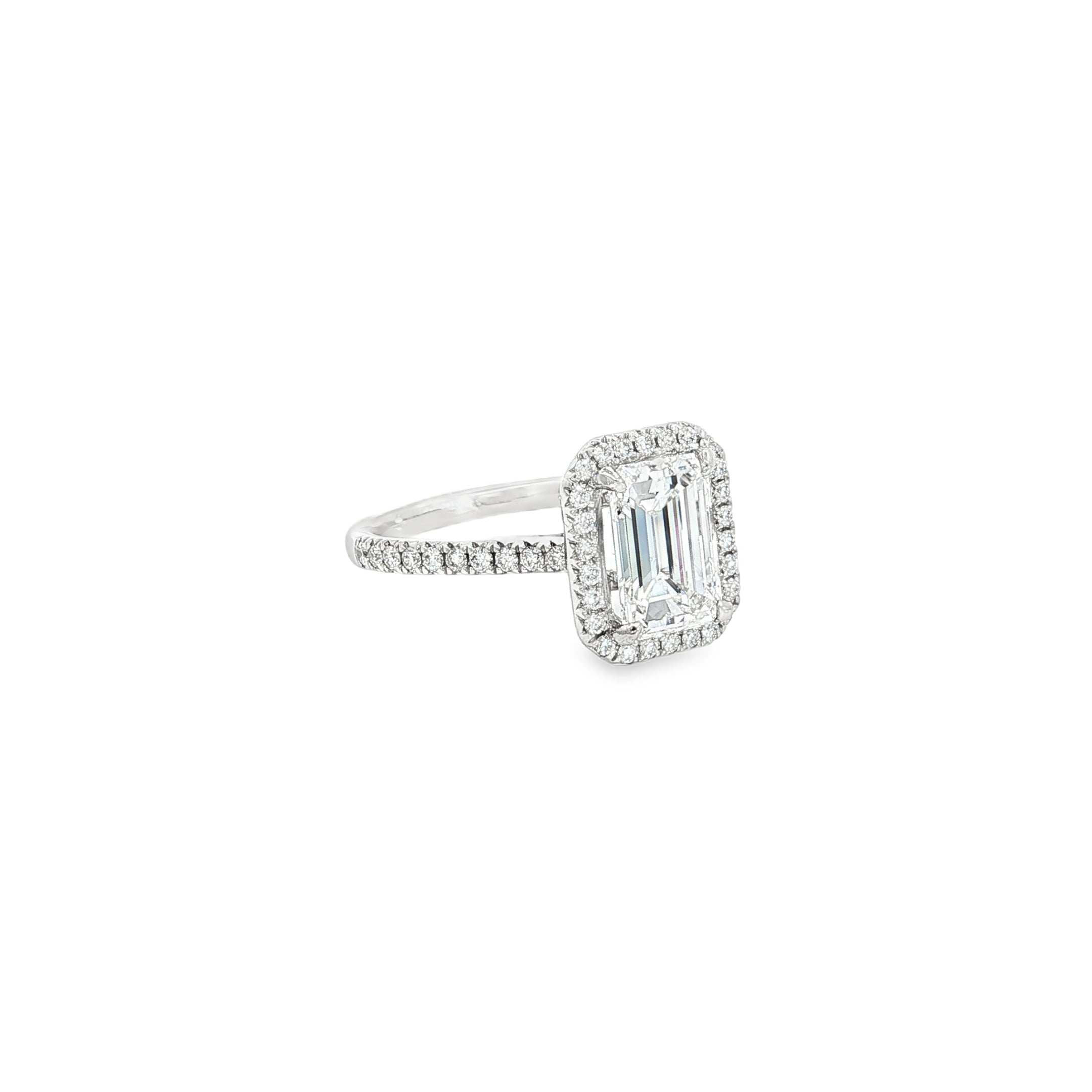 Platinum emerald cut diamond ring with halo and diamond-set shoulders.