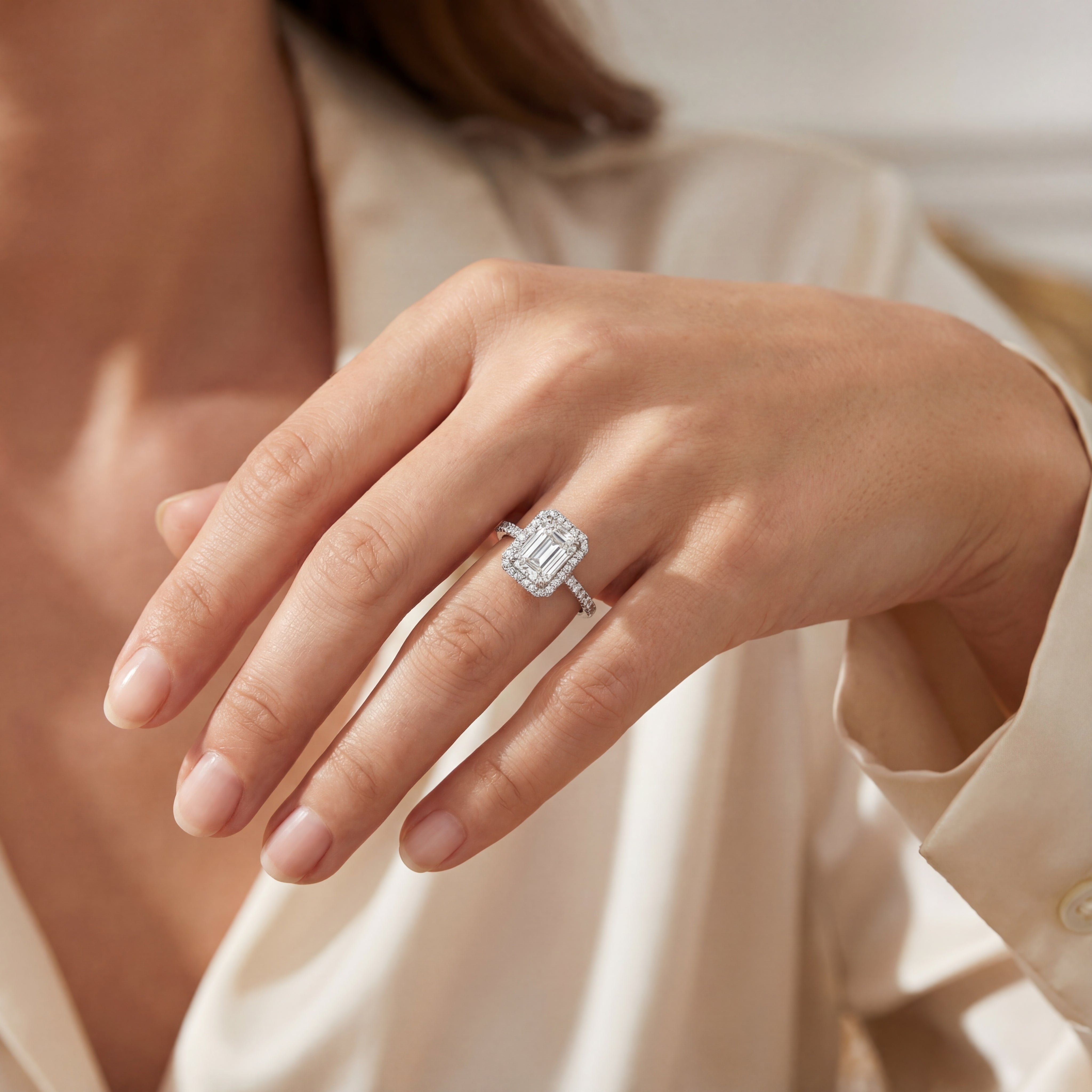 Platinum emerald cut diamond ring with halo and diamond-set shoulders.