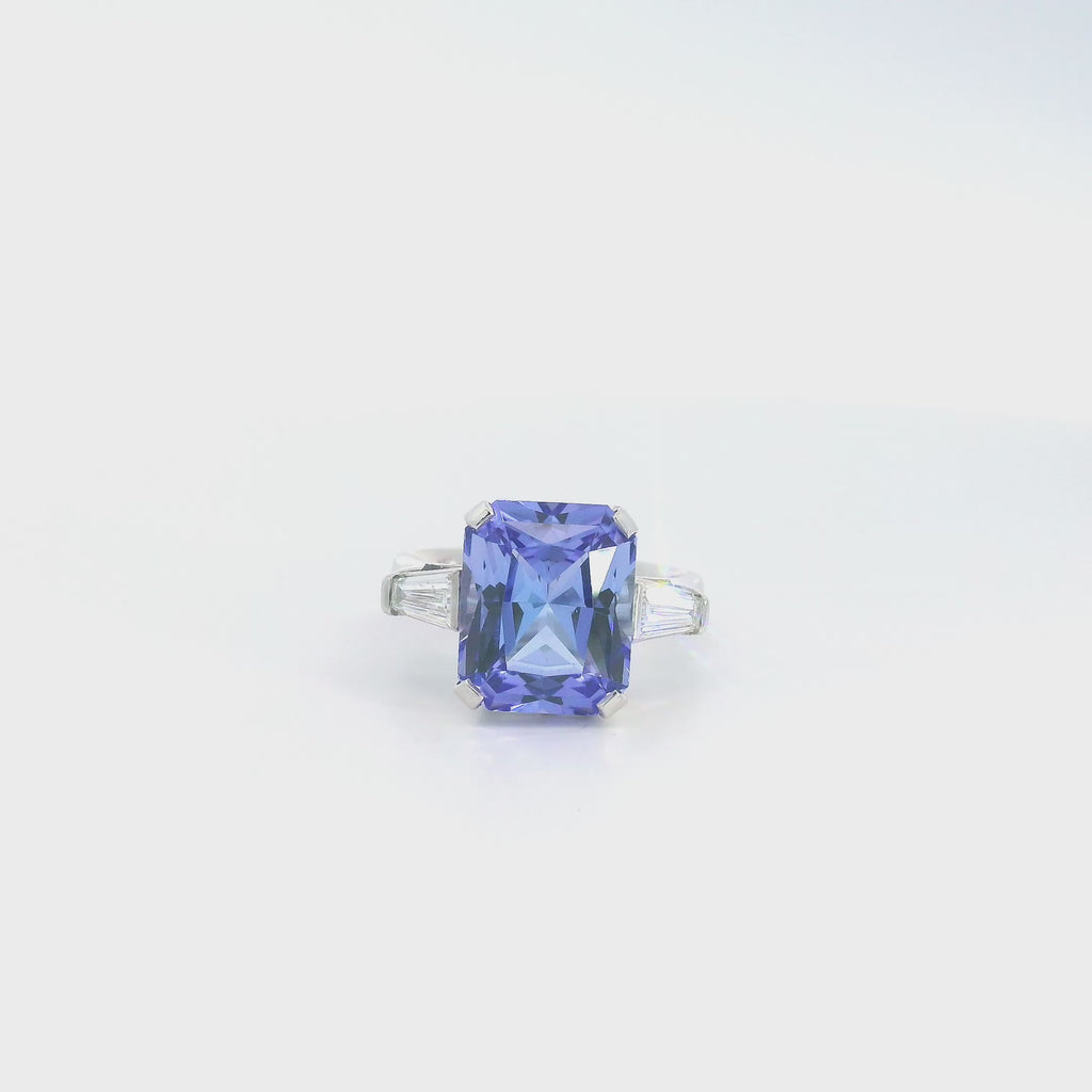 18ct white gold ring featuring a 6.99ct radiant cut tanzanite with two tapered baguette cut diamonds in a tiered three-stone setting.