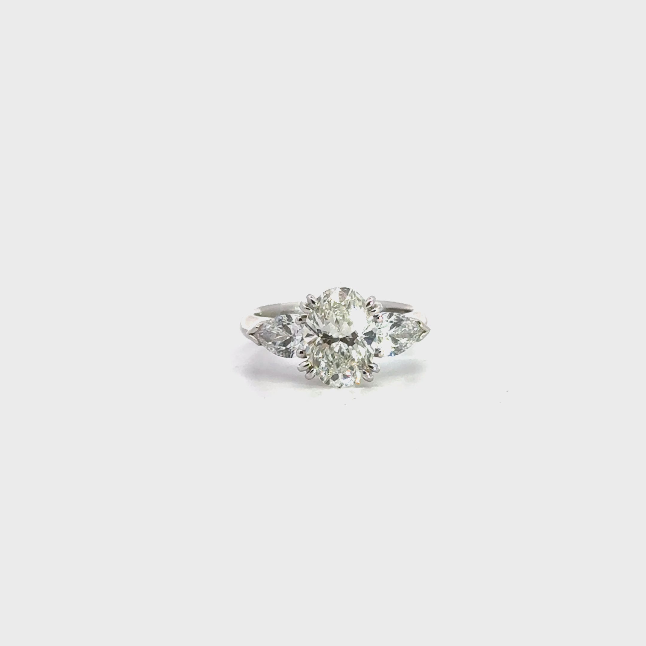 18ct white gold three stone diamond ring featuring a 2.17ct oval centre diamond with pear cut diamond side stones in tiered cap-and-claw settings.
