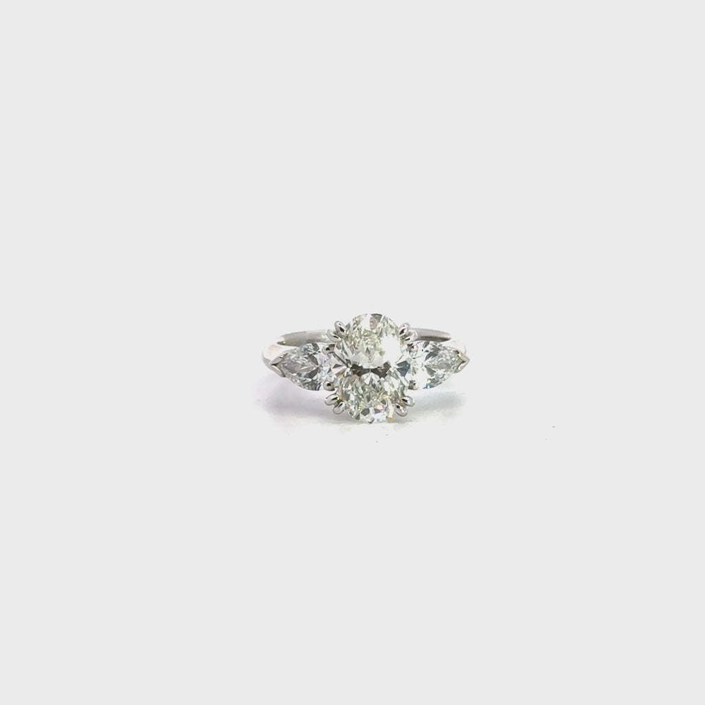 18ct white gold three stone diamond ring featuring a 2.17ct oval centre diamond with pear cut diamond side stones in tiered cap-and-claw settings.