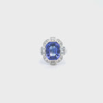 18ct white gold ring featuring a 5.11ct emerald cut tanzanite framed by emerald and round brilliant cut diamonds in a detailed halo setting with upswept shoulders.