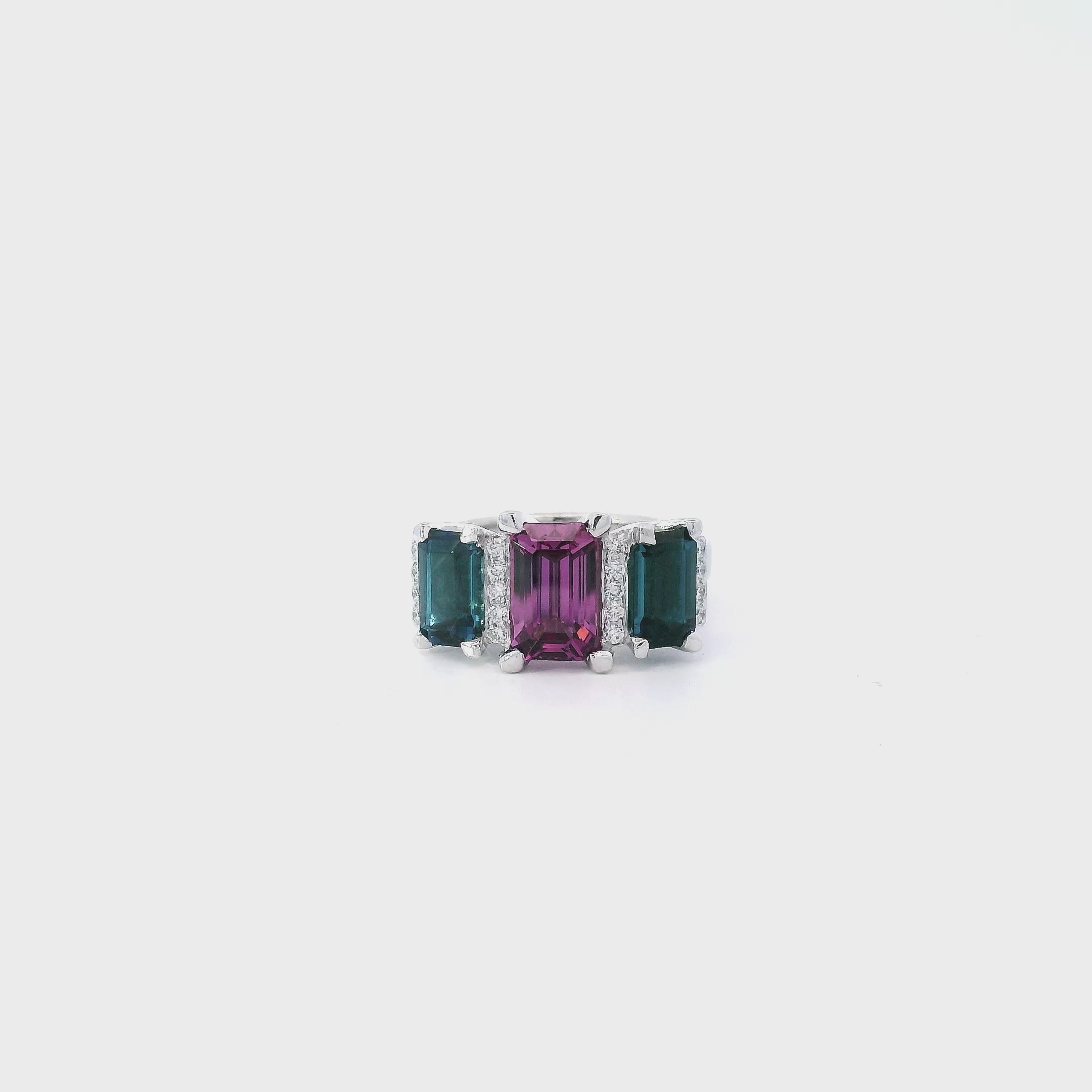 18ct white gold ring featuring a 2.11ct emerald cut purple-pink Malaia garnet with two greenish-blue tourmalines and diamond-set tiered claw and bar details.