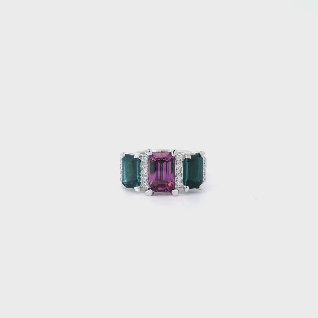 18ct white gold ring featuring a 2.11ct emerald cut purple-pink Malaia garnet with two greenish-blue tourmalines and diamond-set tiered claw and bar details.