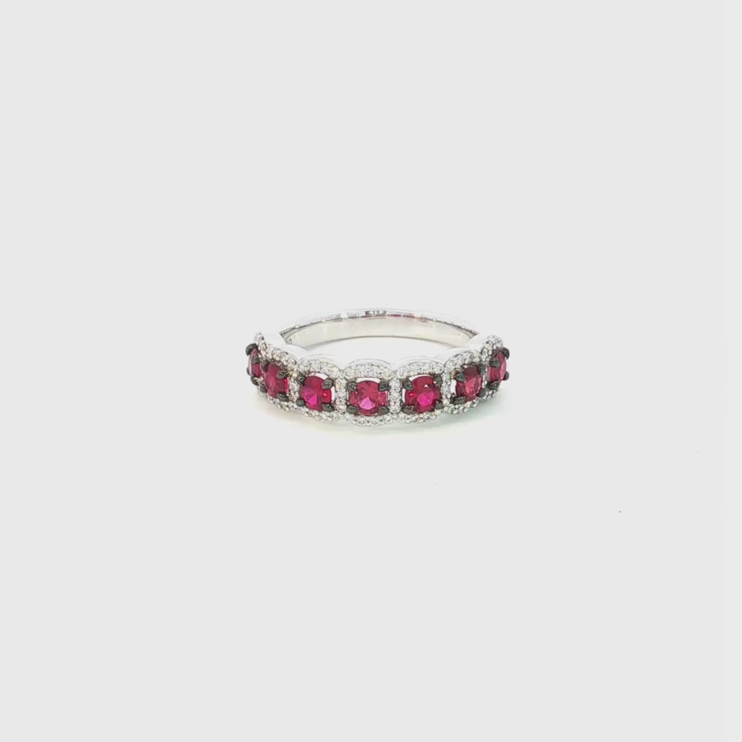 18ct white gold ruby and diamond cluster ring featuring seven round rubies with black rhodium claws and a cushion-shaped diamond halo surround.