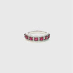 18ct white gold ruby and diamond cluster ring featuring seven round rubies with black rhodium claws and a cushion-shaped diamond halo surround.