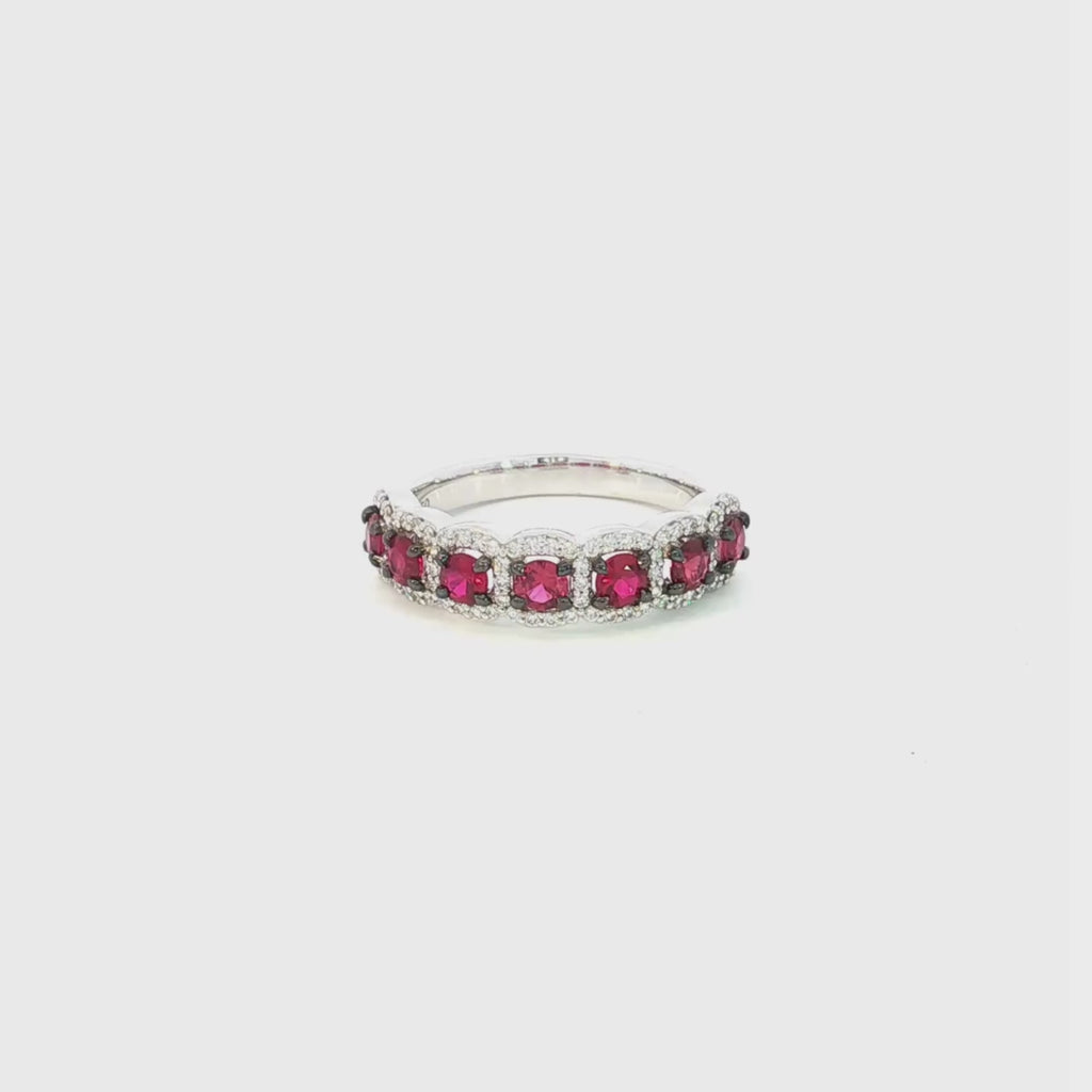 18ct white gold ruby and diamond cluster ring featuring seven round rubies with black rhodium claws and a cushion-shaped diamond halo surround.