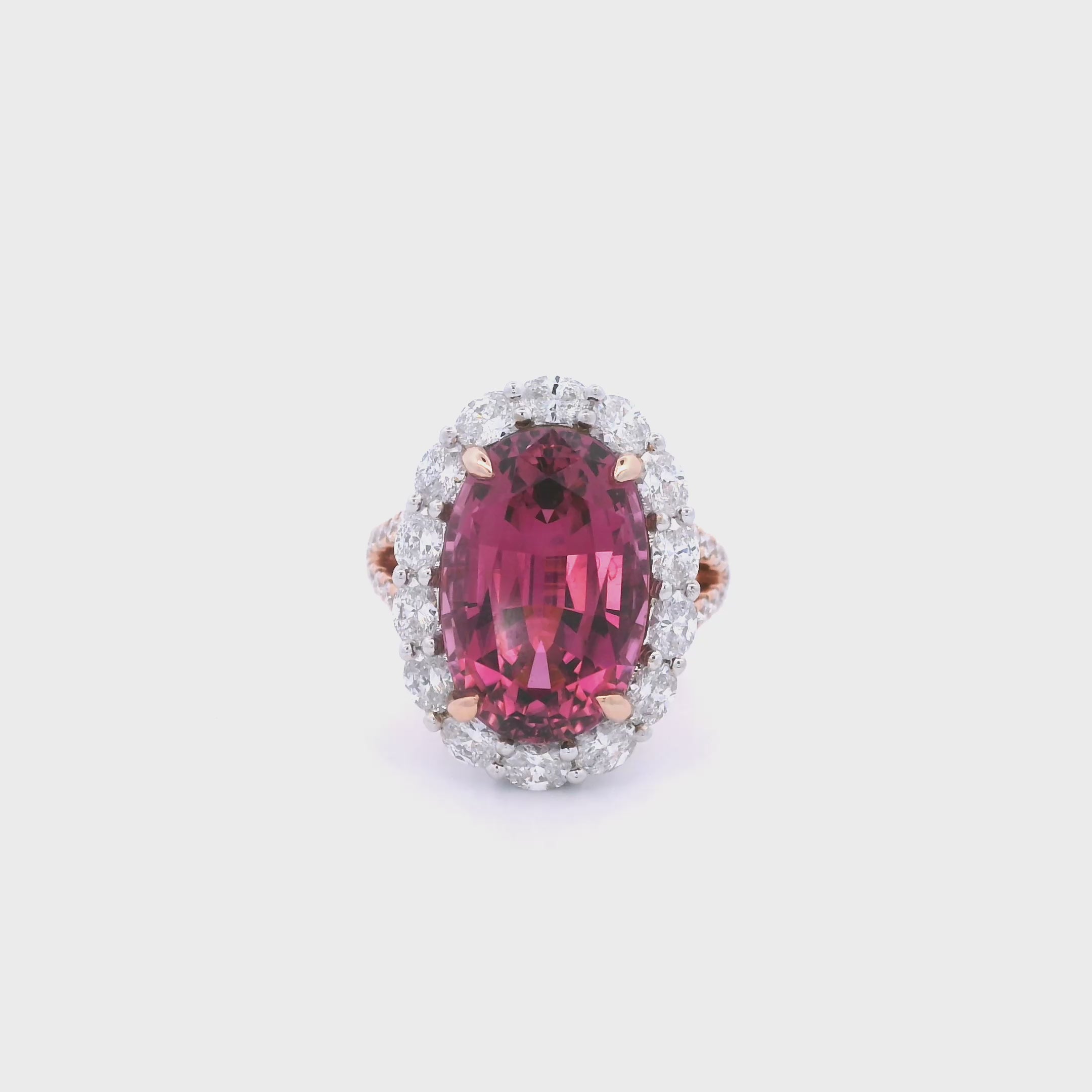 18ct rose and white gold ring featuring a 9.25ct oval pink tourmaline surrounded by a halo of diamonds, with rubies bead set into the undercarriage and split claw shoulders.