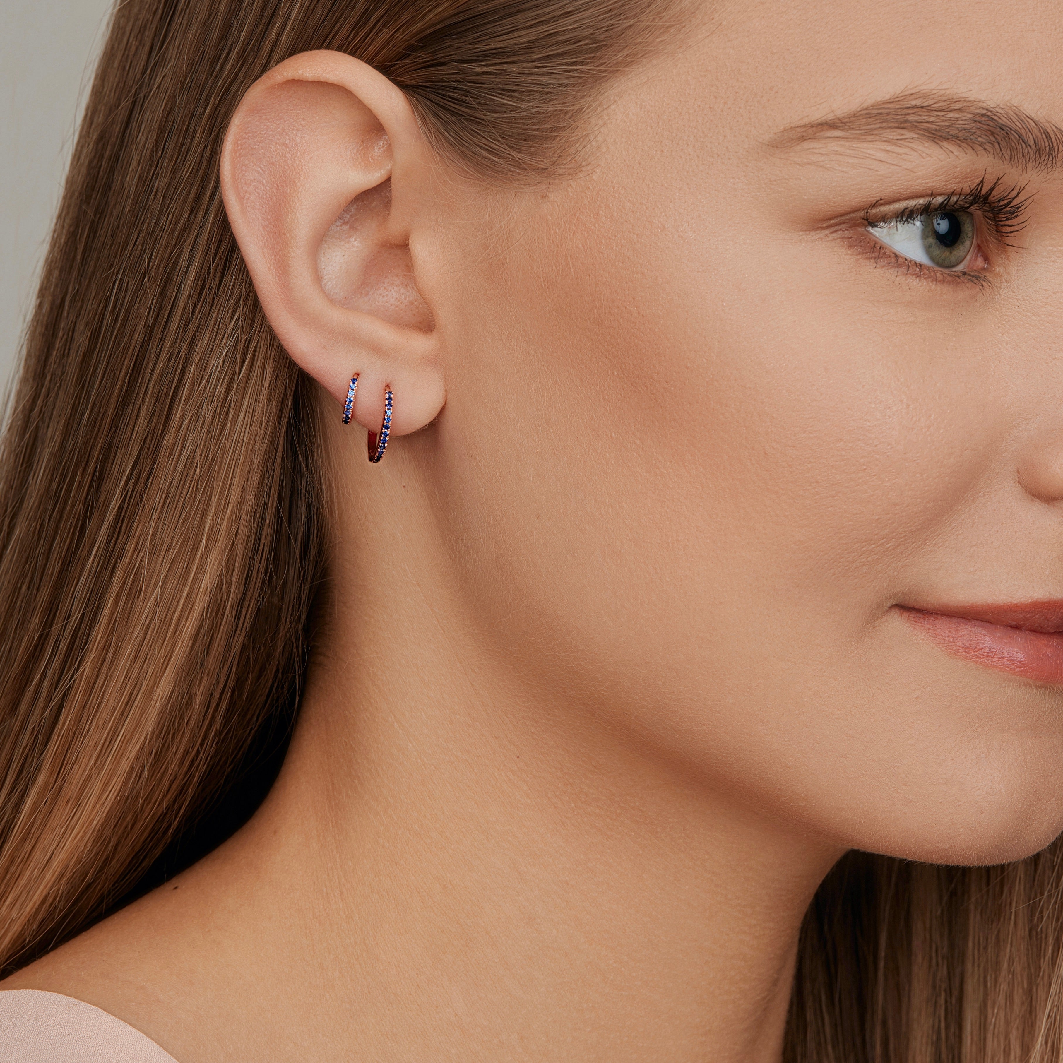 18ct rose gold sapphire huggie earrings with claw-set sapphires around the front and inside back.