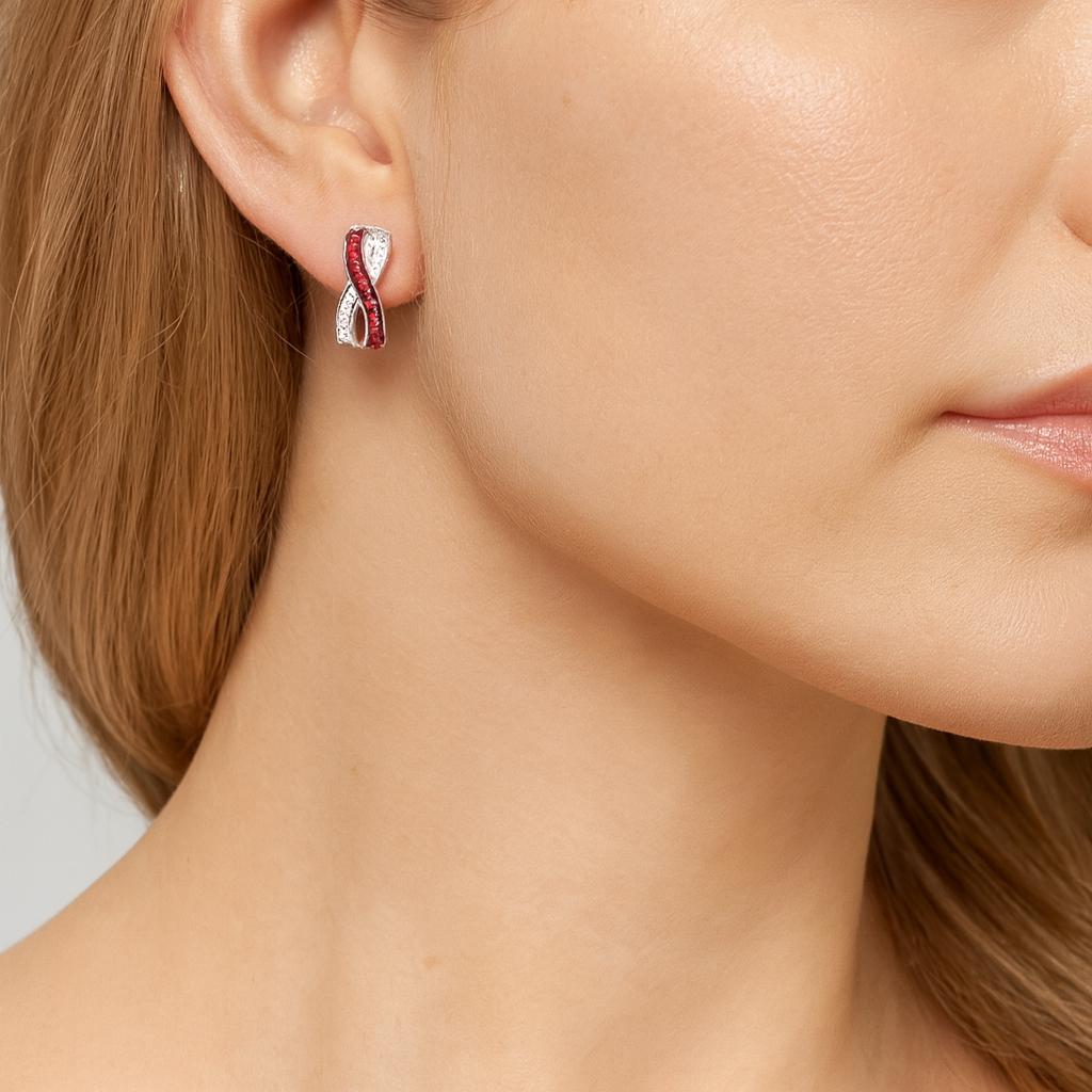 18ct white gold ruby and diamond earrings featuring a curved “X”-shaped crossover front with rubies set in black rhodium and white diamonds in alternating rows.