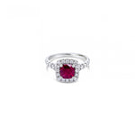 18ct white gold ring featuring a 1.06ct cushion-cut ruby in a four-claw setting with a cushion-shaped diamond halo and claw-set shoulders.